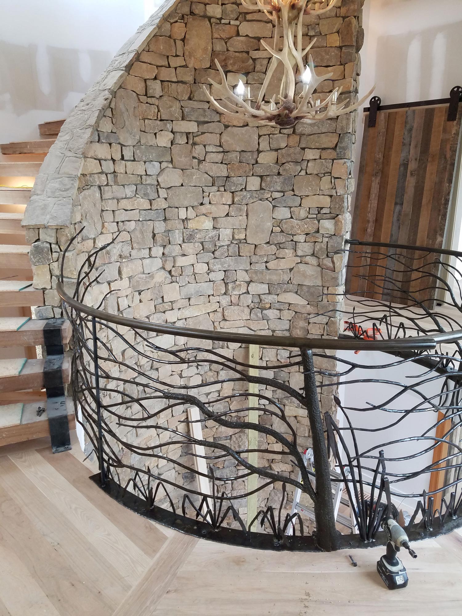 Open, circular staircase with stacked stone walls, antler chandelier, custom live edge metal works with branch motif Open, circular staircase with stacked stone walls, antler chandelier, custom live edge metal works with branch motif